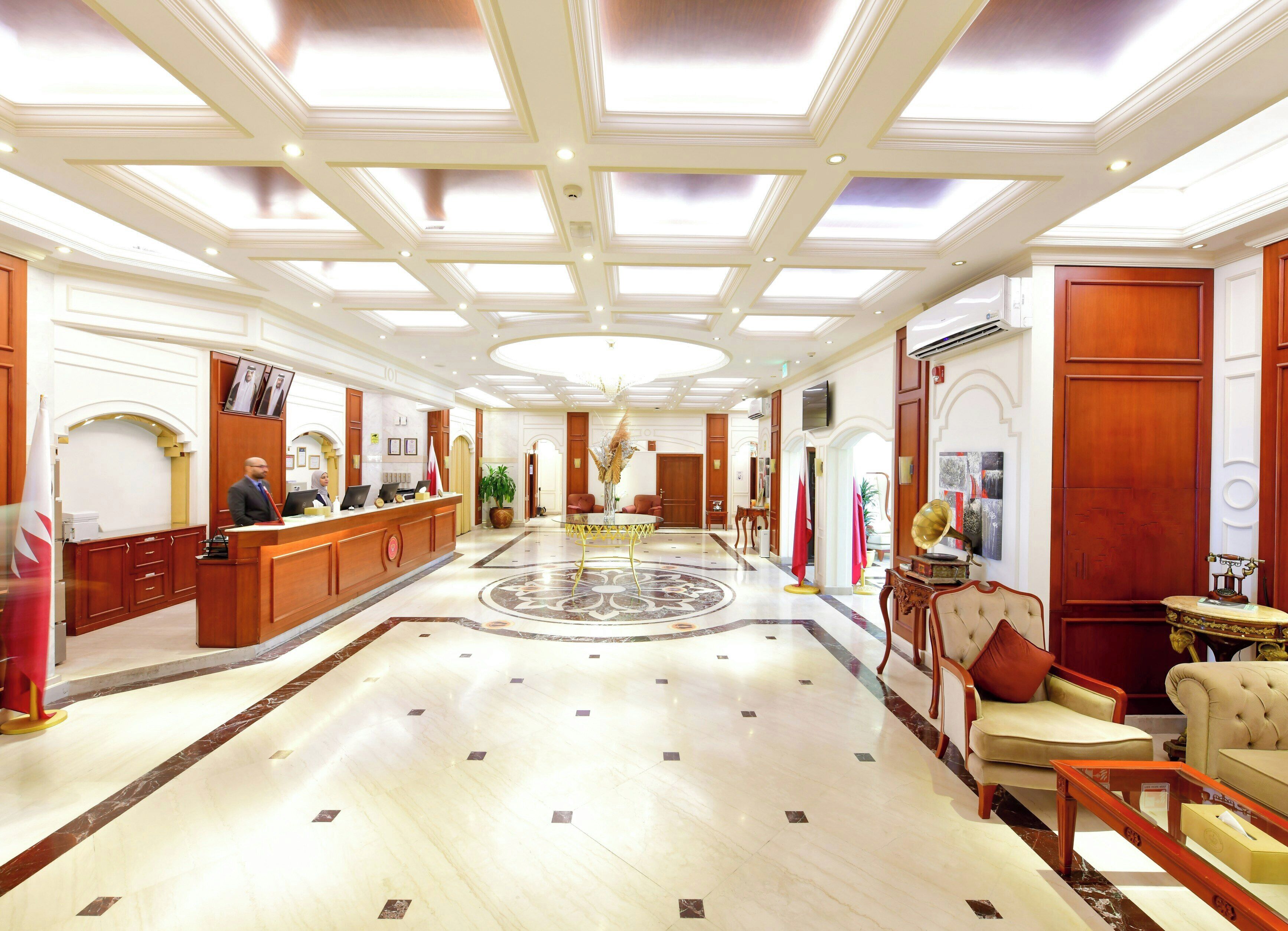A spacious lobby with a central circular floor design, a reception desk, and a seating area with armchairs and a sofa.