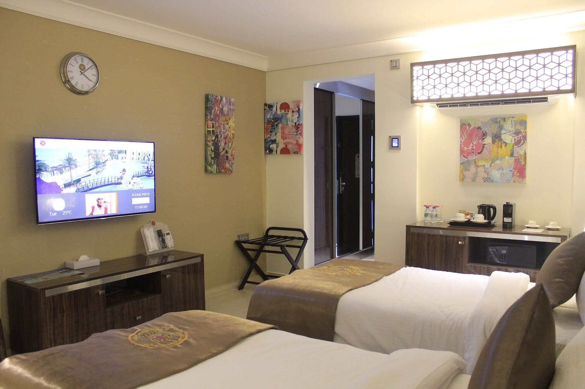Een hotelkamer met twee bedden, een televisie waarop een strandafbeelding te zien is, een klok en kunst aan de wanden.