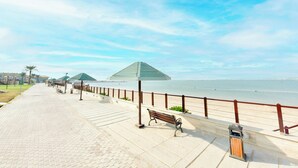 Ein gepflasterter Weg mit Bänken, einem Mülleimer und einer Geländer entlang eines Strandes.