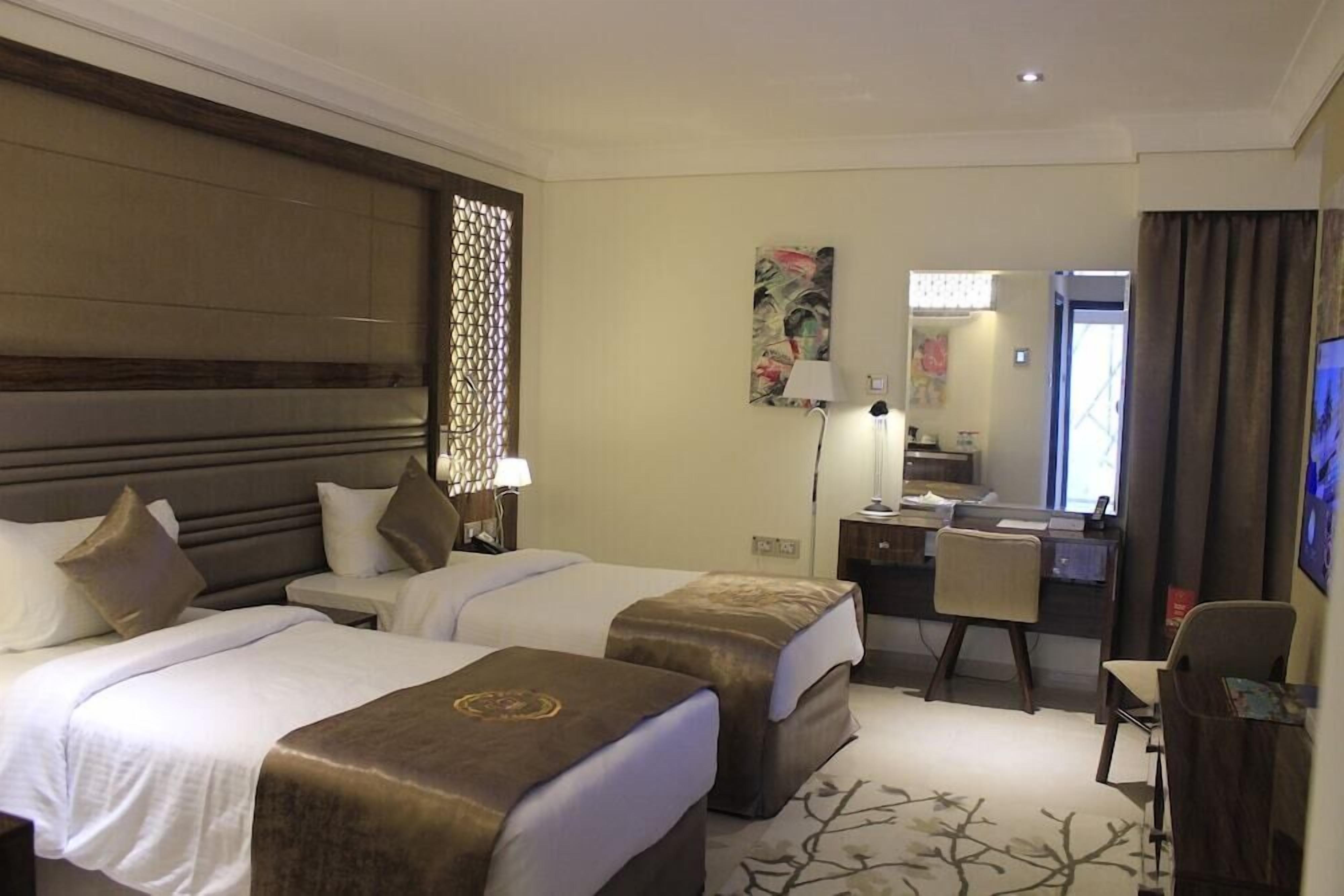 A hotel room with two beds, a desk, a chair, a TV, and a bathroom visible through an open door.