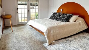 A bedroom with a bed, a wooden nightstand, a large window, and a door. - Quaint 1-bedroom Unit  w/ Hottub in Uptown Sedona (Sedona)