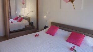 Een slaapkamer met een grote spiegel, een bed met roze kussens, een nachtkastje en een wandlamp.