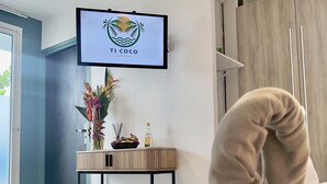 Hotelkamer met een bed, een aan de muur bevestigde televisie waarop een logo staat, een klein tafeltje met decoratieve objecten en een houten kledingkast.