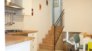 A kitchen with a gas stove, wooden cabinets, a stainless steel range hood, and a staircase leading to a dining area with a chair. - [Historic Center] A/C e WiFi in the Heart of Le Marche region (Lapedona)