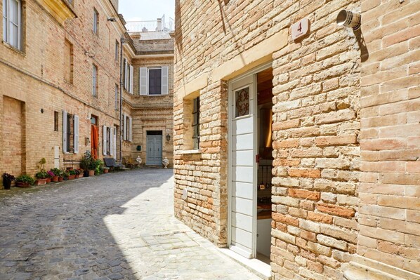 A narrow cobblestone street flanked by historic buildings with a brick facade and a door with a window.