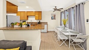 A modern kitchen with granite countertops, wooden cabinets, and a built-in dishwasher. There is a dining area with a white table and chairs, and a ceiling fan above. - Cozy n Serene 12mins to Downtown LA (Alhambra)