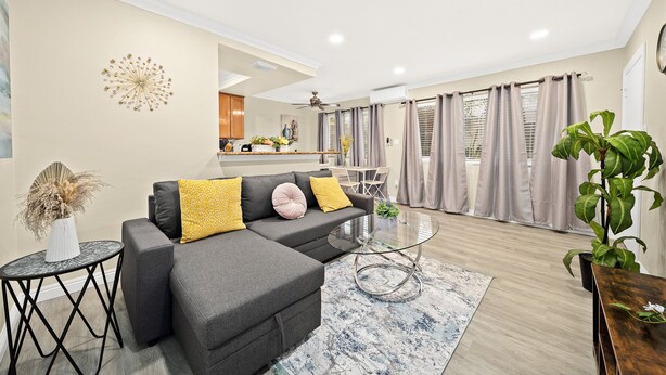 A modern living room with a grey sectional sofa, a glass coffee table, and a large potted plant. - Cozy n Serene 12mins to Downtown LA (Alhambra)