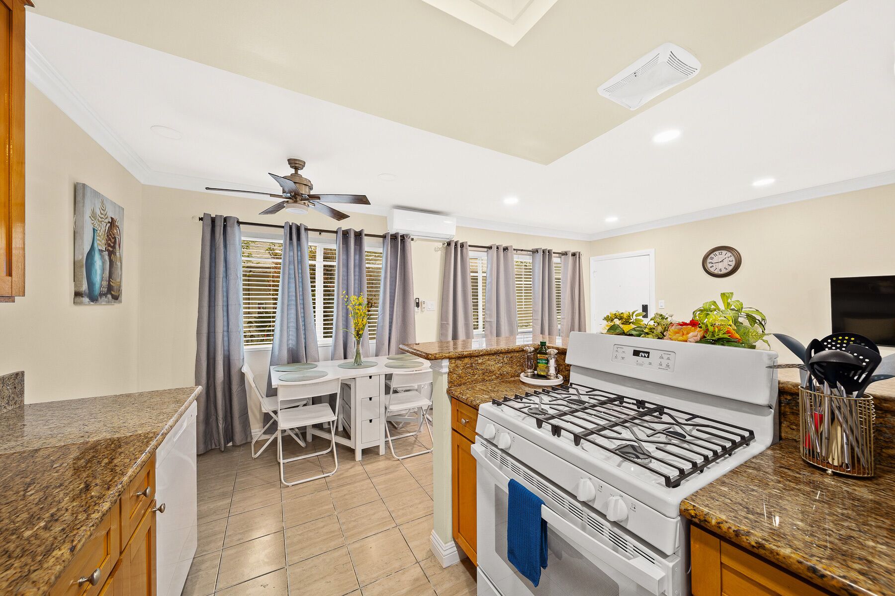 A modern kitchen with a gas stove, a dining area with a table and chairs, and a ceiling fan.