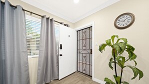 A hallway with a wooden floor, a potted plant, a door with a decorative metal gate, and a wall-mounted clock. - Cozy n Serene 12mins to Downtown LA (Alhambra)