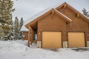 Surrounded by serene winter landscapes, this cabin features a symmetrical facade with two garage doors and a central entrance.