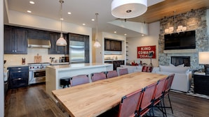 A modern kitchen with a central island, dark wooden cabinets, stainless steel appliances, and a stone fireplace. - Luxury Big Sky Ski Retreat - Moonlight Basin (Big Sky)