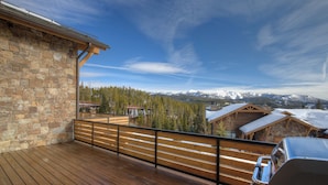 A wooden deck with a stone wall, overlooking a mountainous landscape with snow-capped peaks. - Luxury Big Sky Ski Retreat - Moonlight Basin (Big Sky)