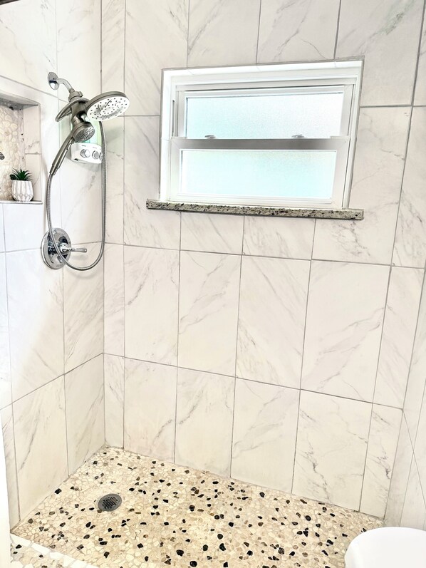 A shower with a handheld showerhead and a wall-mounted control panel.