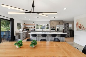 A modern kitchen with a central island, bar stools, and a dining table with potted plants.