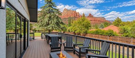 A deck with outdoor seating and a fire feature, overlooking a mountainous landscape.