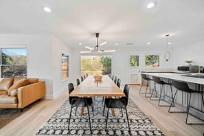 A modern kitchen with a long dining table, black chairs, and a kitchen island with bar stools.