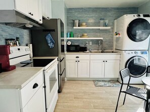 A compact kitchen with white cabinets, a built-in oven, a microwave, a sink, and a washing machine.