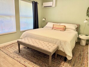 A bedroom with a bed, bench, bedside table, and a window with blinds.