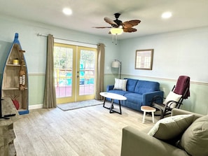 A living room with a blue sofa, a white coffee table, a ceiling fan, and a wooden shelf with a sign.