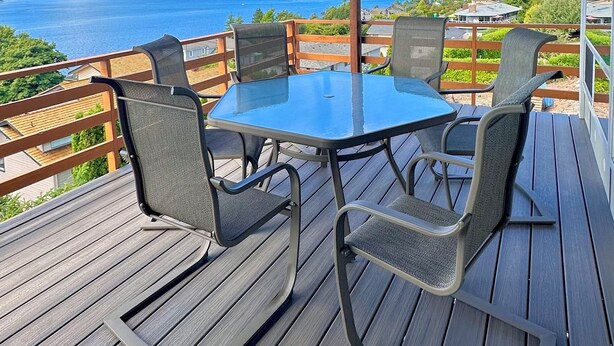 Een overdekt terras met een tafel en stoelen, met uitzicht op een prachtig waterlandschap en verre landschappen.