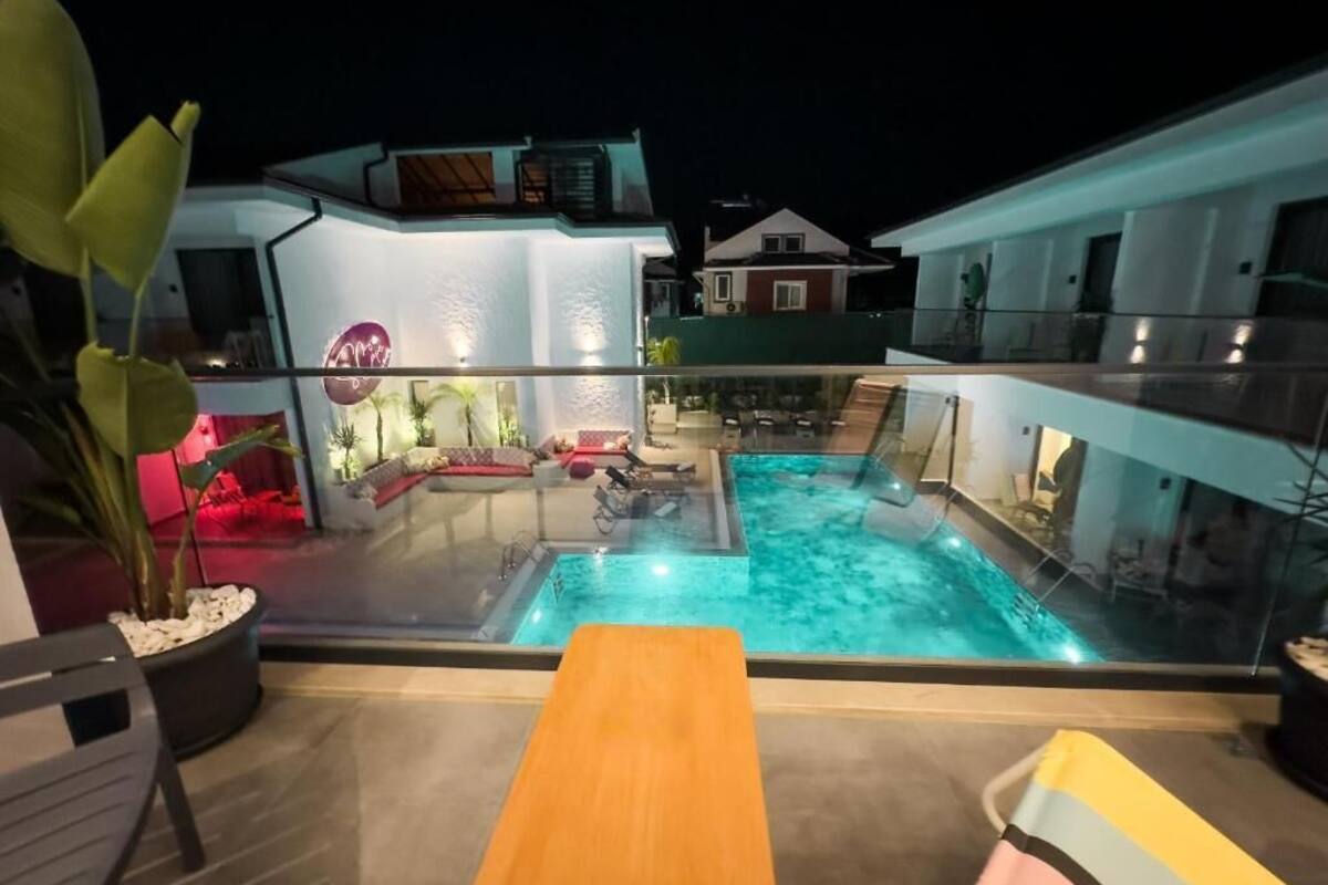 Un espace piscine aménagé sur le toit, doté d’une balustrade en verre, d’une terrasse en bois et d’un coin salon avec un canapé rouge et une table.