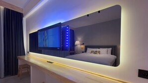 A modern hotel room with a large TV mounted on a wall, a bedside table, a bed with white bedding, and a nightstand with a lamp. - S-Cape Hotel Fethiye (Fethiye)
