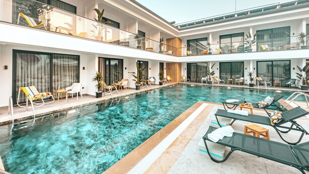 A modern indoor swimming pool with multiple levels of balconies, lounge chairs, and potted plants. - S-Cape Hotel Fethiye (Fethiye)