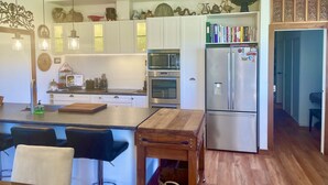 A modern kitchen with white cabinets, stainless steel appliances, and a wooden island with bar stools. - Ballygelvar (Cambridge)