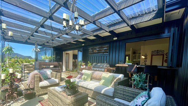 A covered outdoor seating area with wicker furniture, a glass ceiling, and a grill. - Ballygelvar (Cambridge)
