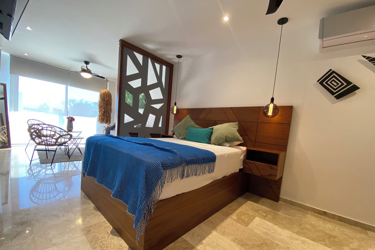 A modern bedroom with a wooden bed, a decorative partition, a hanging light fixture, and a view of the outdoors.