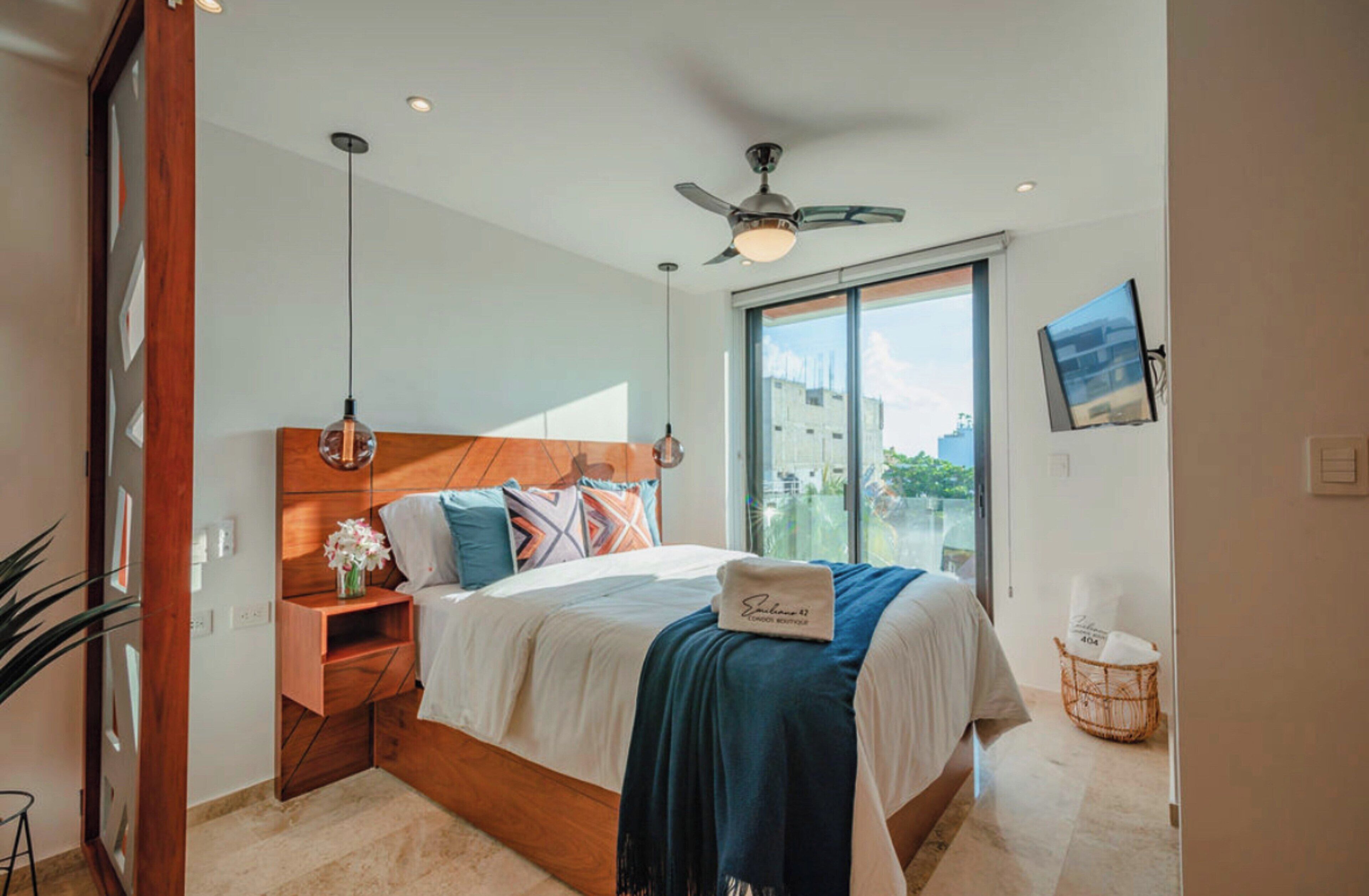 A bedroom with a bed, bedside table, nightstand, and a window with a view.