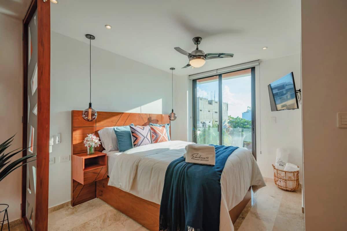 A bedroom with a bed, bedside table, nightstand, and a window with a view.