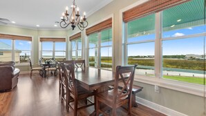 A spacious dining area with a large wooden table and chairs, large windows with views of the outdoors, and a chandelier. - Waterfront Oasis w/ Dock, Sleeps 12 (Bay St. Louis)