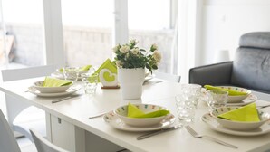 Una mesa de comedor dispuesta con platos, tazones, vasos y cubiertos, con un jarrón blanco con flores en el centro.