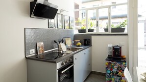 Una cocina moderna con horno empotrado, microondas y cafetera. Hay plantas en macetas en el alféizar de la ventana y una estación de café colorida.