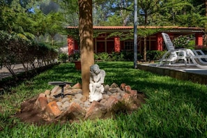 A garden with a statue, a tree, and a building with red brick walls and a tiled roof.