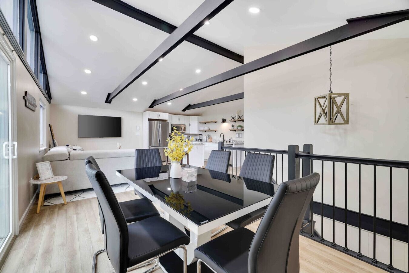 Un espace repas moderne avec une table à plateau en verre, des chaises noires et un vase rempli de fleurs jaunes.