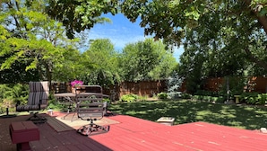 Une terrasse rouge avec une table et des chaises, entourée d’une végétation luxuriante et d’arbres.