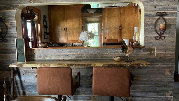 Une cuisine rustique avec des meubles en bois, un coin bar et deux tabourets de bar en cuir.