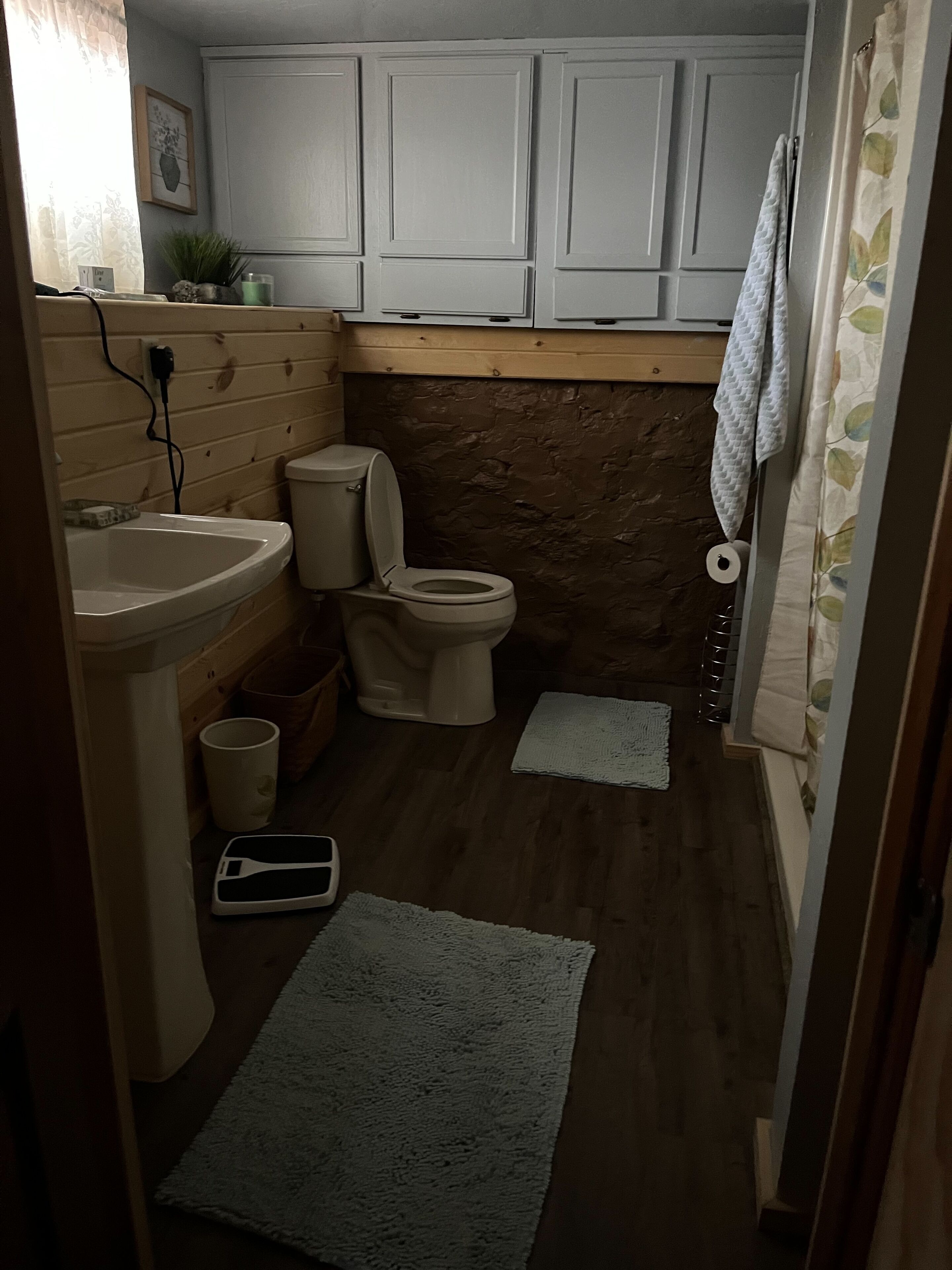 Et lille badeværelse med vask, toilet og en mindre måtte på gulvet.