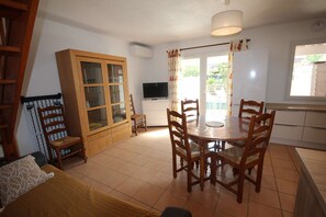 A cozy living room with a dining area, wooden cabinets, a TV, and a window with a view.