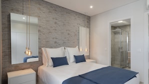 Een moderne slaapkamer met een groot bed, een nachtkastje, een spiegel en een inloopdouche.
