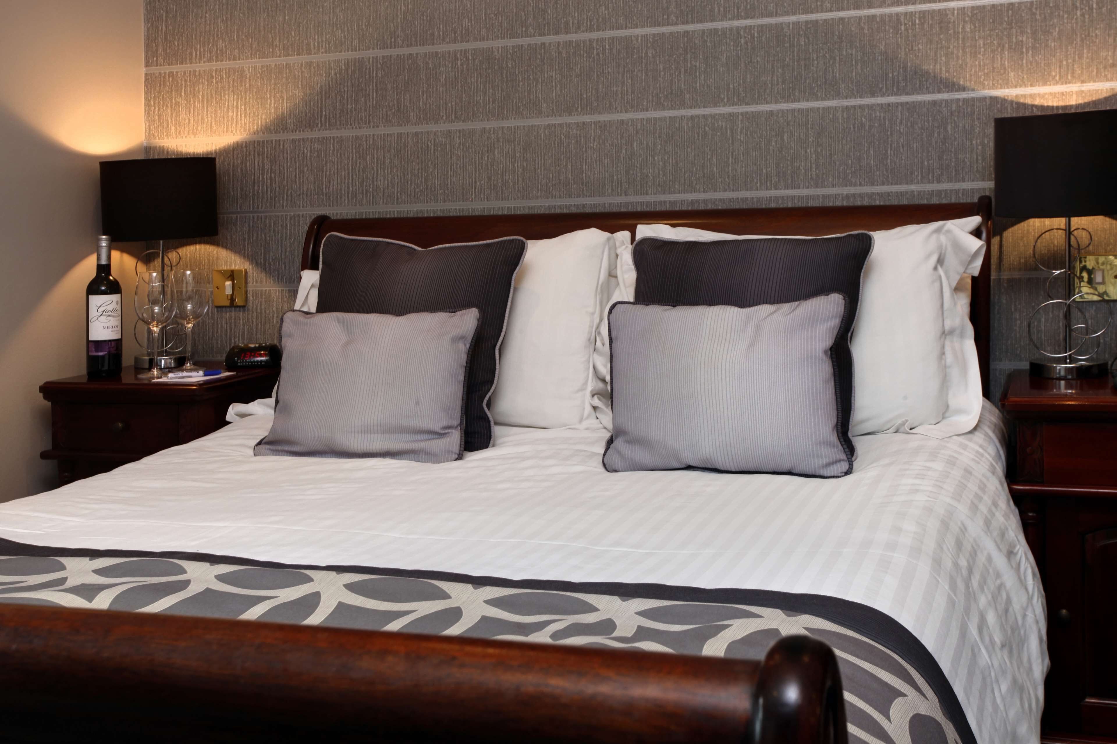 A neatly made bed with a patterned bedspread, two bedside tables with lamps, and a bottle of wine on one table.