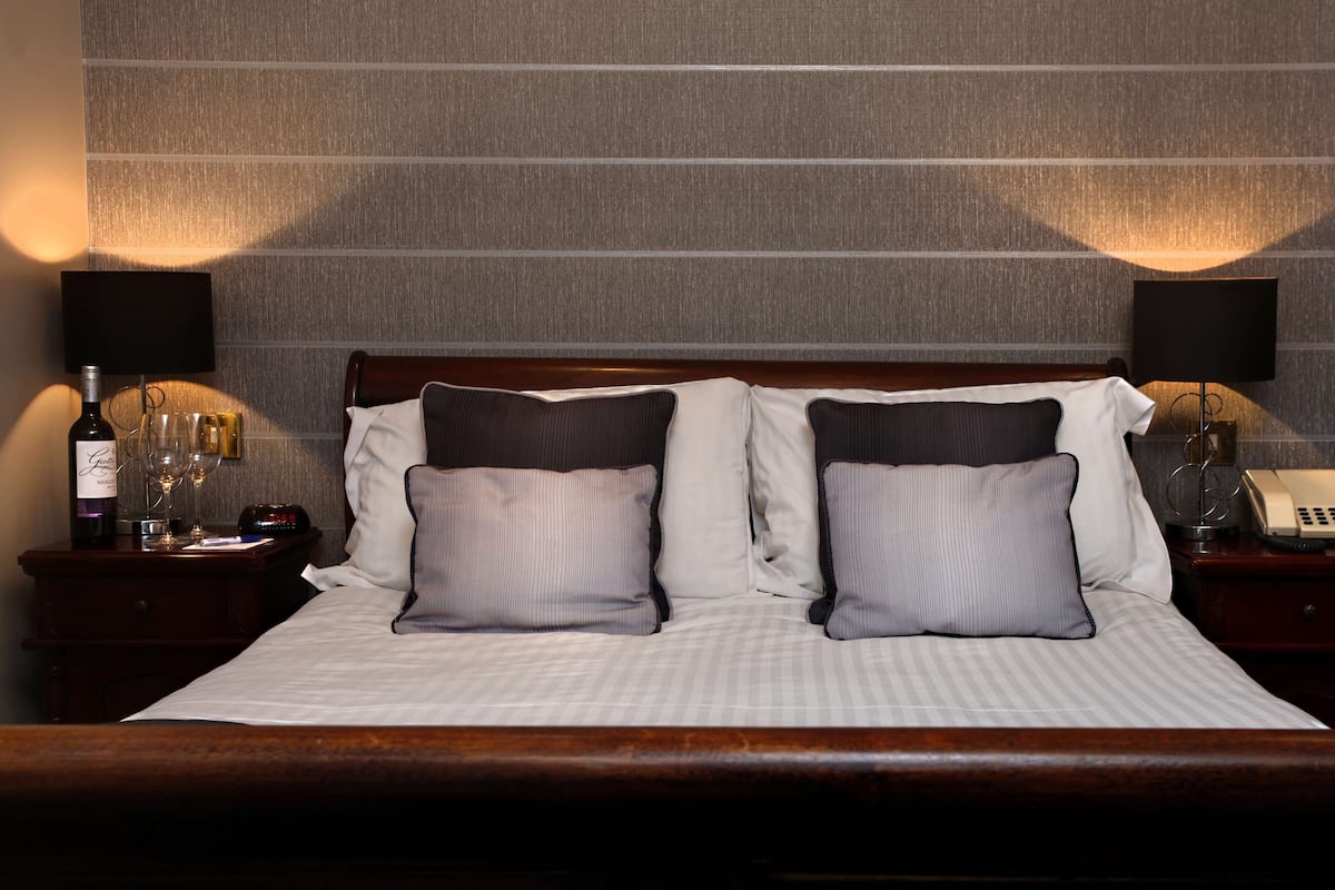 A hotel room with a large bed, two bedside tables, a wine bottle, and glasses on one side.