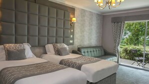 A hotel room with two beds, a sofa, a chandelier, and a view of greenery through the window. - Dryfesdale Hotel, Bw Signature Collection (Lockerbie)