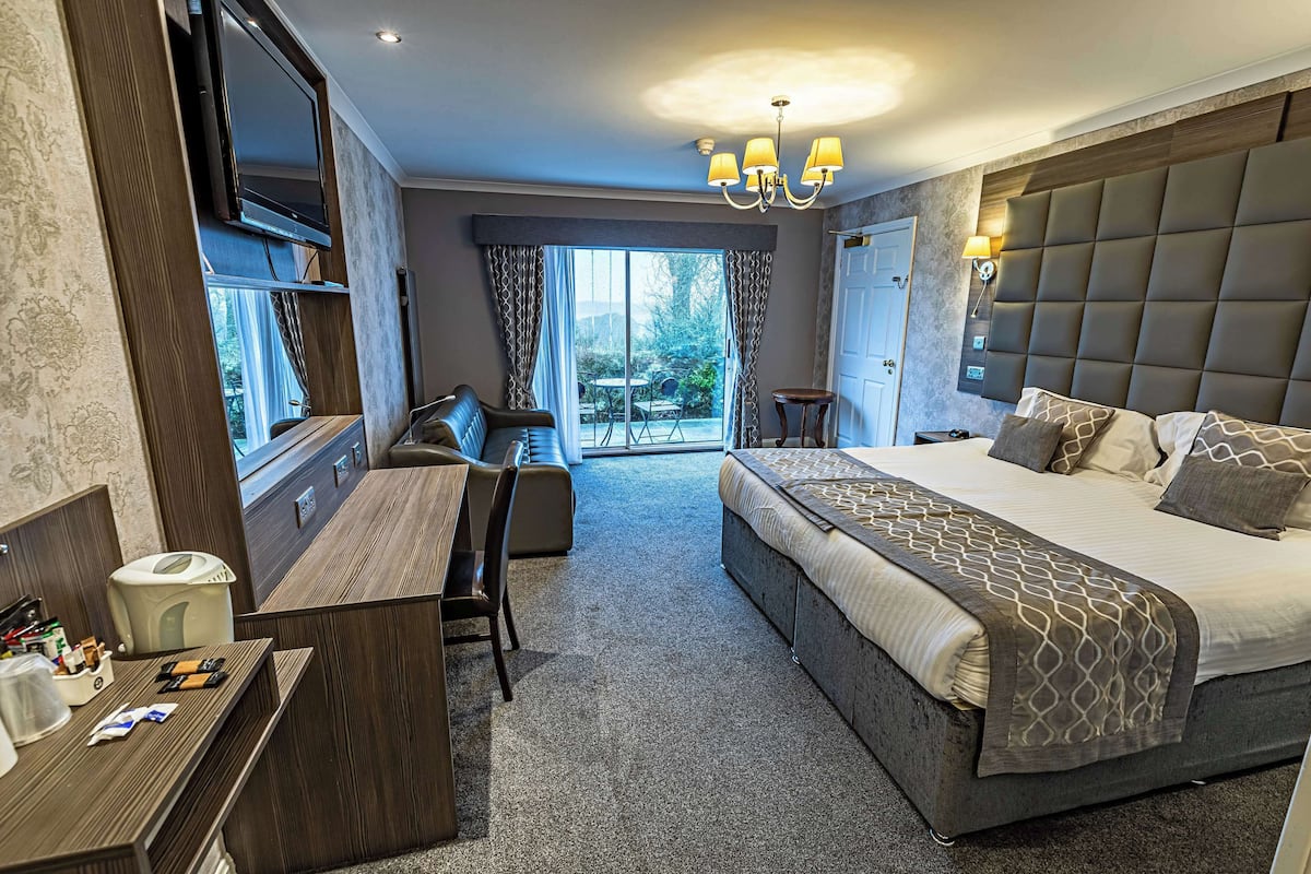 A hotel room with a bed, a desk, a chair, a TV, and a view of the outdoors.