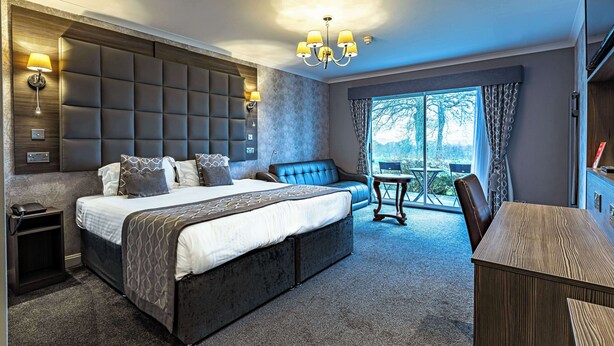 A modern bedroom with a large bed, a sofa, a desk, and a view of the outdoors. - Dryfesdale Hotel, Bw Signature Collection (Lockerbie)
