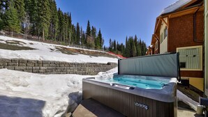 Un jacuzzi en un área exterior nevada con una terraza de madera y un muro de ladrillo.