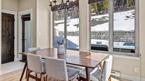 Un comedor con mesa de madera y cuatro sillas, ventanas amplias con vista a un paisaje nevado y una araña.