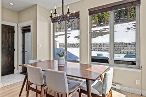 Un coin repas avec une table en bois et quatre chaises, de grandes fenêtres donnant sur un paysage enneigé et un lustre.